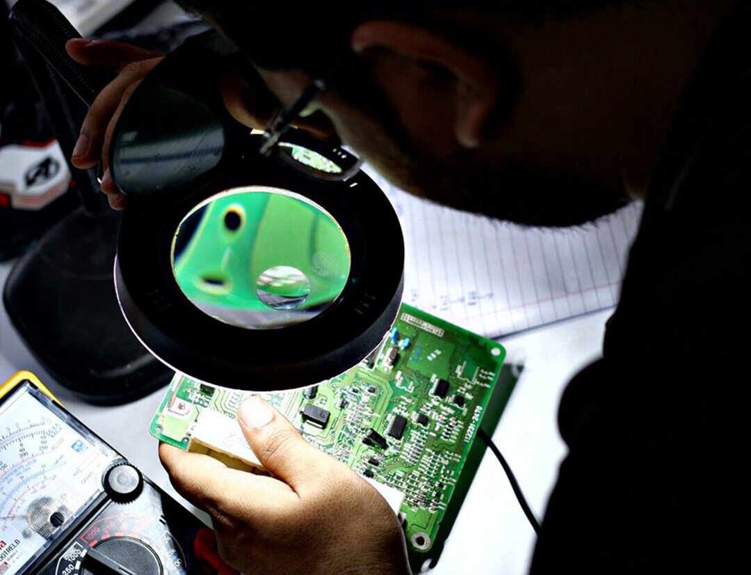 Technician repairing ECU circuit board with soldering iron and diagnostic tools